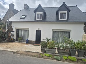Ein zweistöckiges Haus mit dunklem Dach, weißen Wänden und einer kleinen Veranda mit Blumentöpfen.