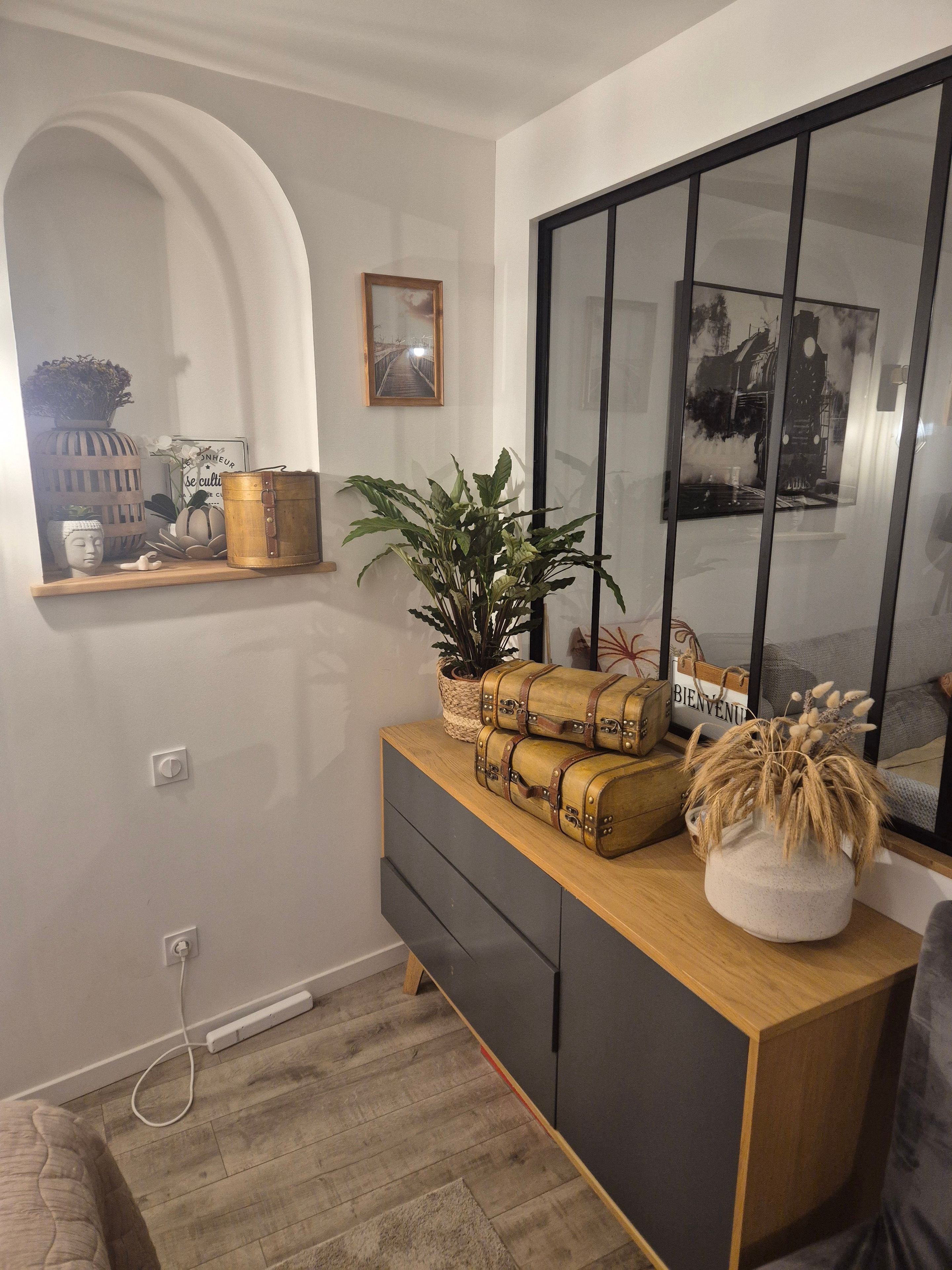 A modern interior with a wooden console table, a potted plant, and a mirror reflecting a clock and a bridge.