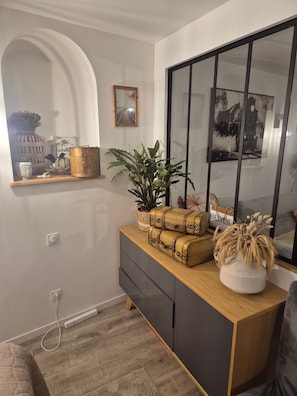 A modern interior with a wooden console table, a potted plant, and a mirror reflecting a clock and a bridge.