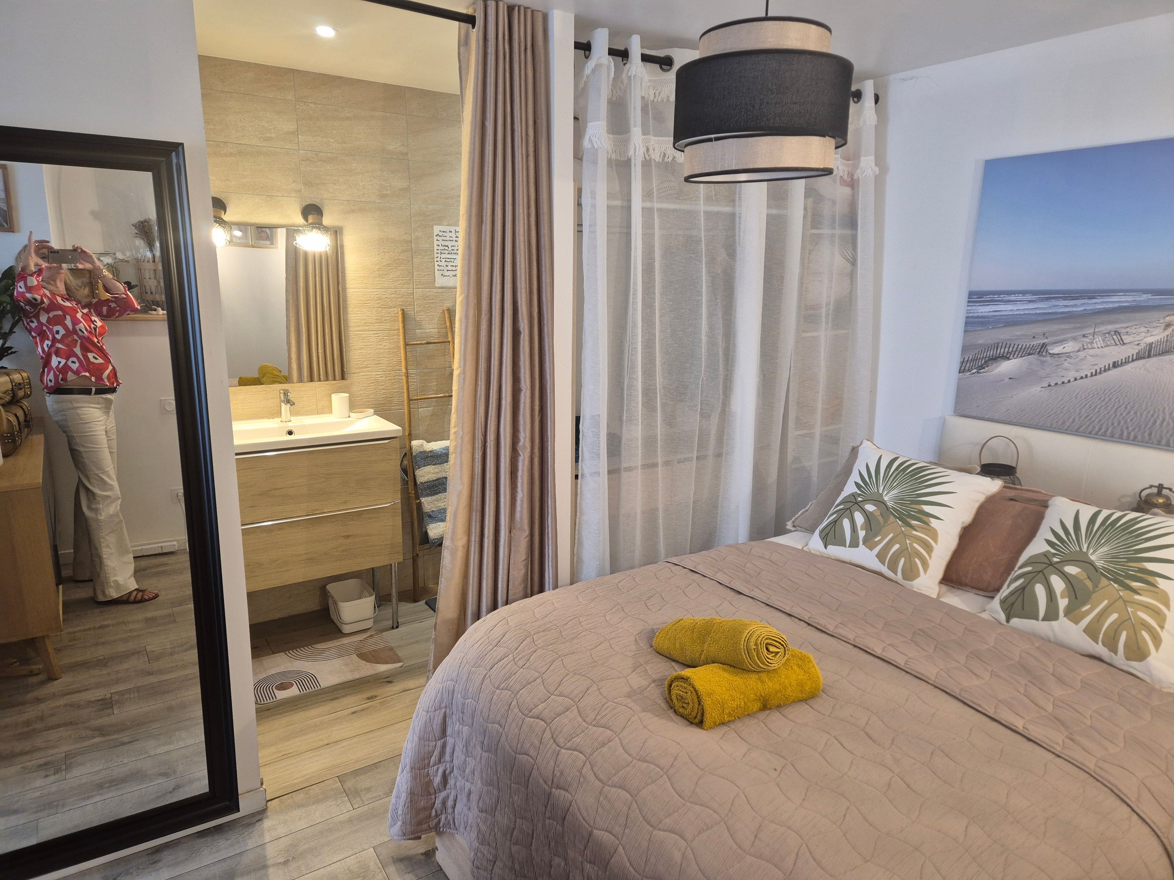 Hotellihuone, jossa on sänky, kylpyhuone ja näkymä rannalle, ja joku ottaa valokuvan.
