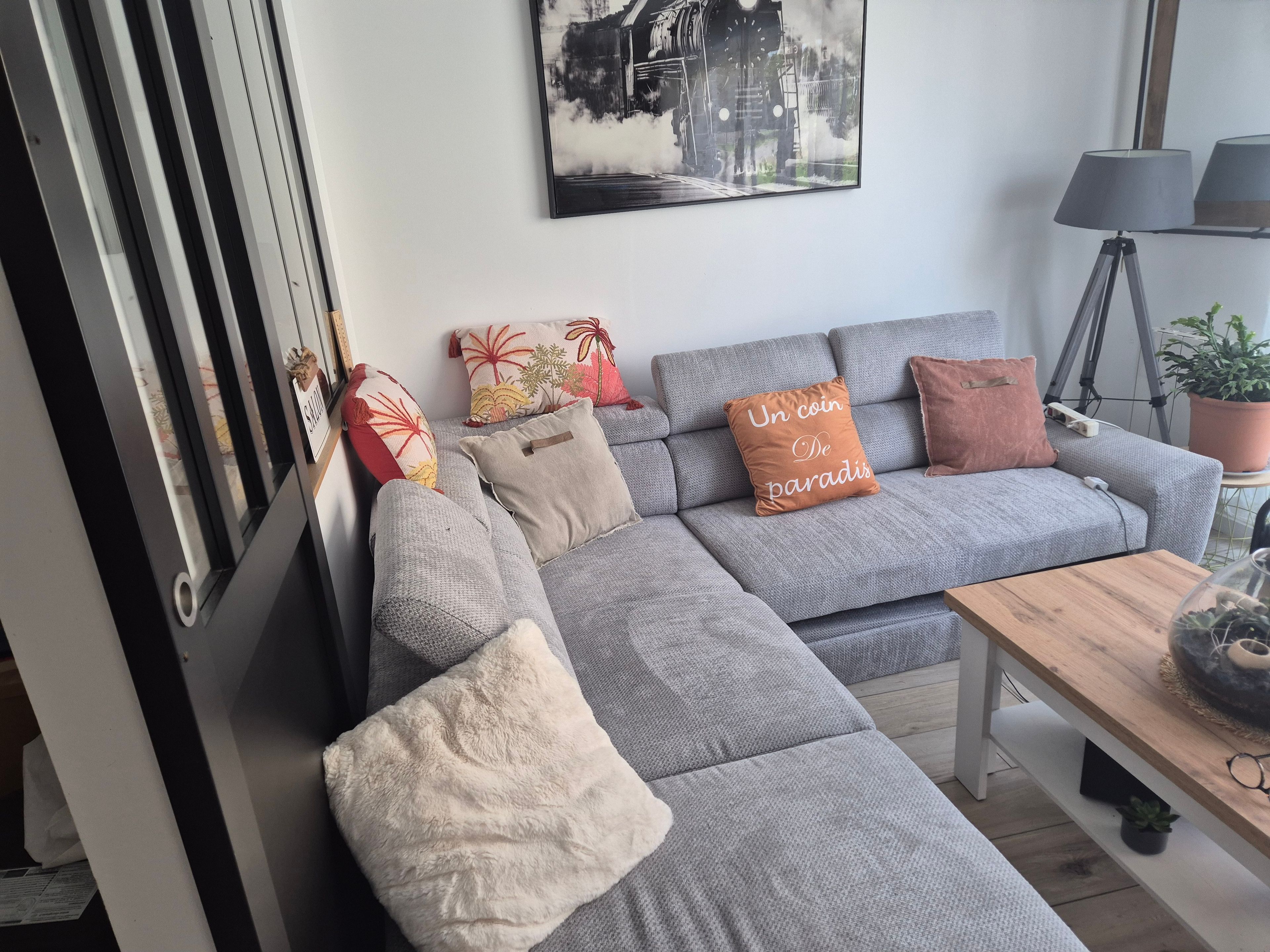 Een moderne woonkamer met een grijze modulaire bank, decoratieve kussens, een ingelijst stadsgezicht, een statief lamp en een houten salontafel.