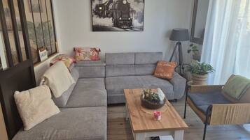 Un salon moderne avec un canapé d’angle gris, une table basse en bois et un tableau en noir et blanc représentant un train, accroché au mur.