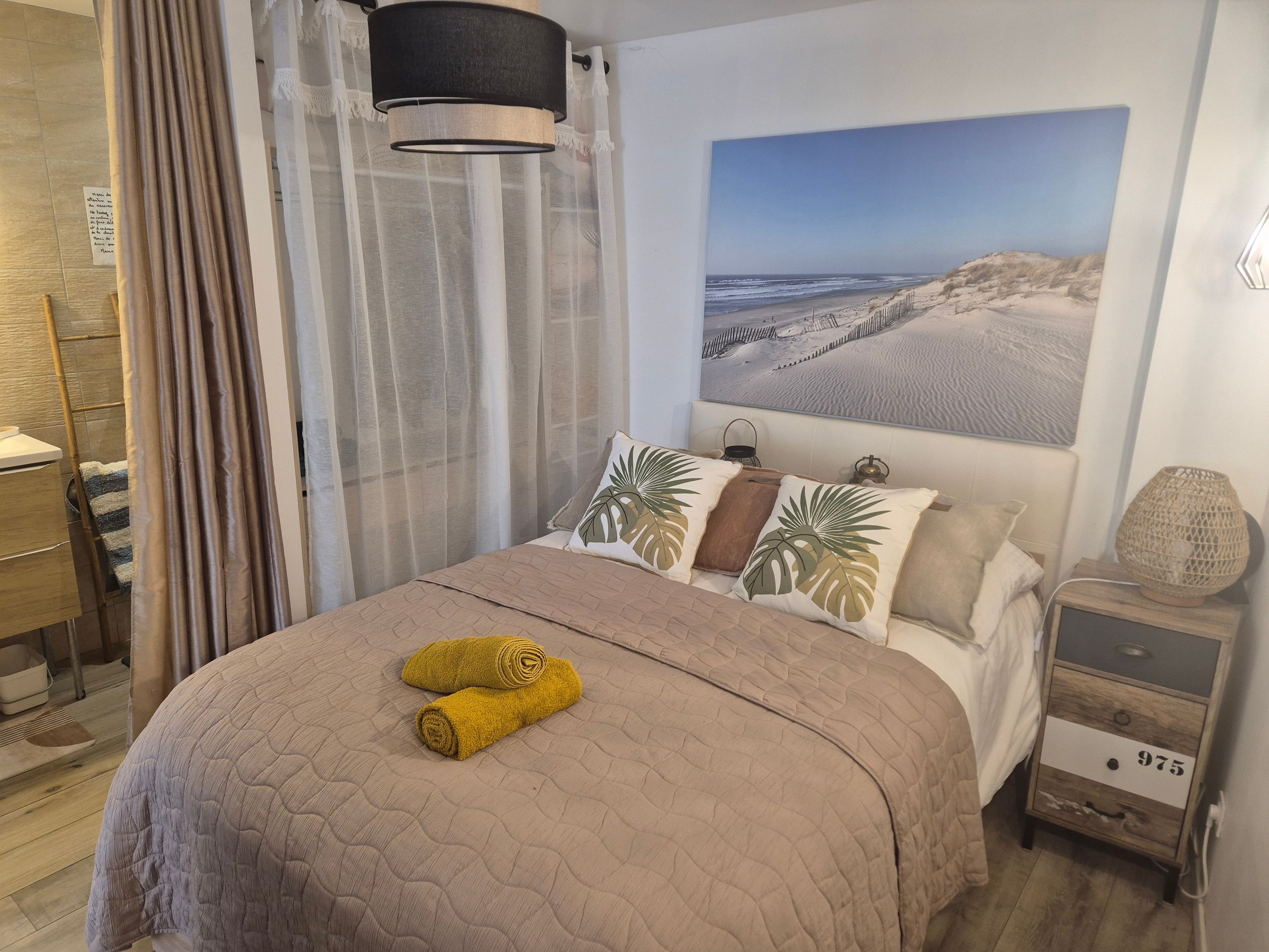 Een slaapkamer met een bed, een nachtkastje, een lamp, een aan de muur hangend schilderij en een raam met gordijnen.