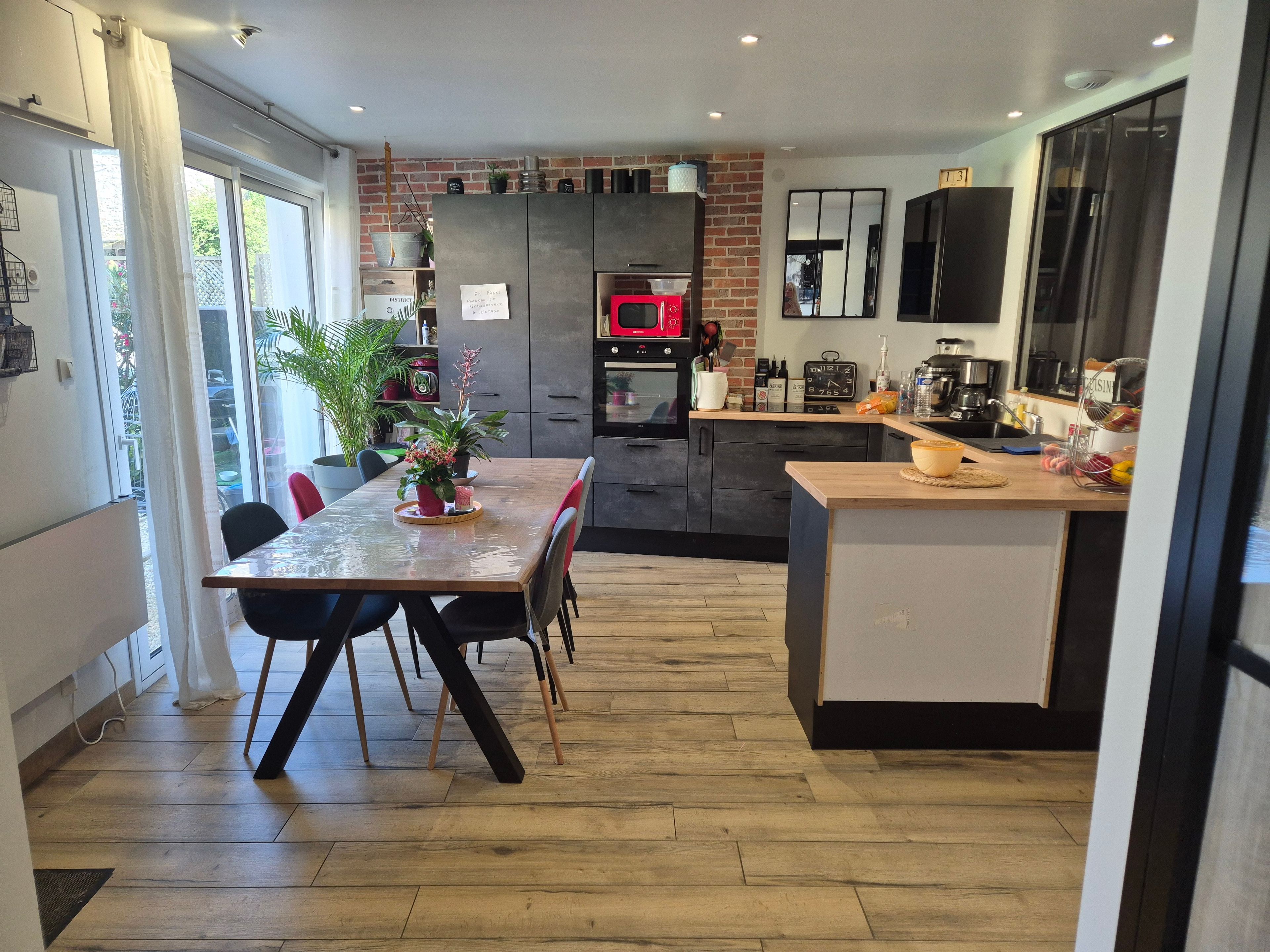 Une cuisine moderne avec un coin repas, comprenant un mur en briques, un micro-ondes rouge et une table à manger en bois.