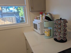 Una cucina con una finestra, un forno a microonde, una macchina per il caffè e una tazza.