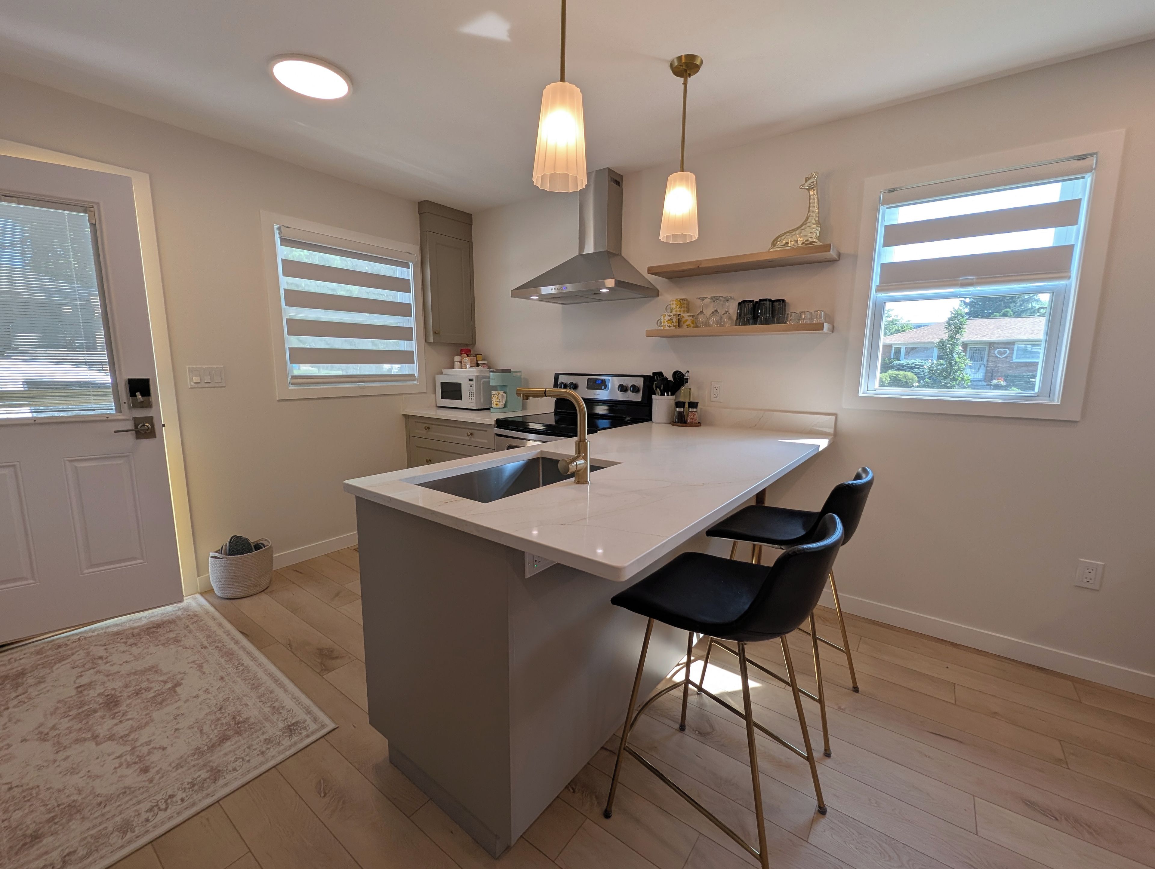 A modern kitchen with a central island, bar stools, pendant lights, and a view of the outside.