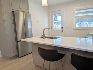 Una cucina moderna con un frigorifero in acciaio inossidabile, un piano di lavoro bianco e due sgabelli da bar neri.