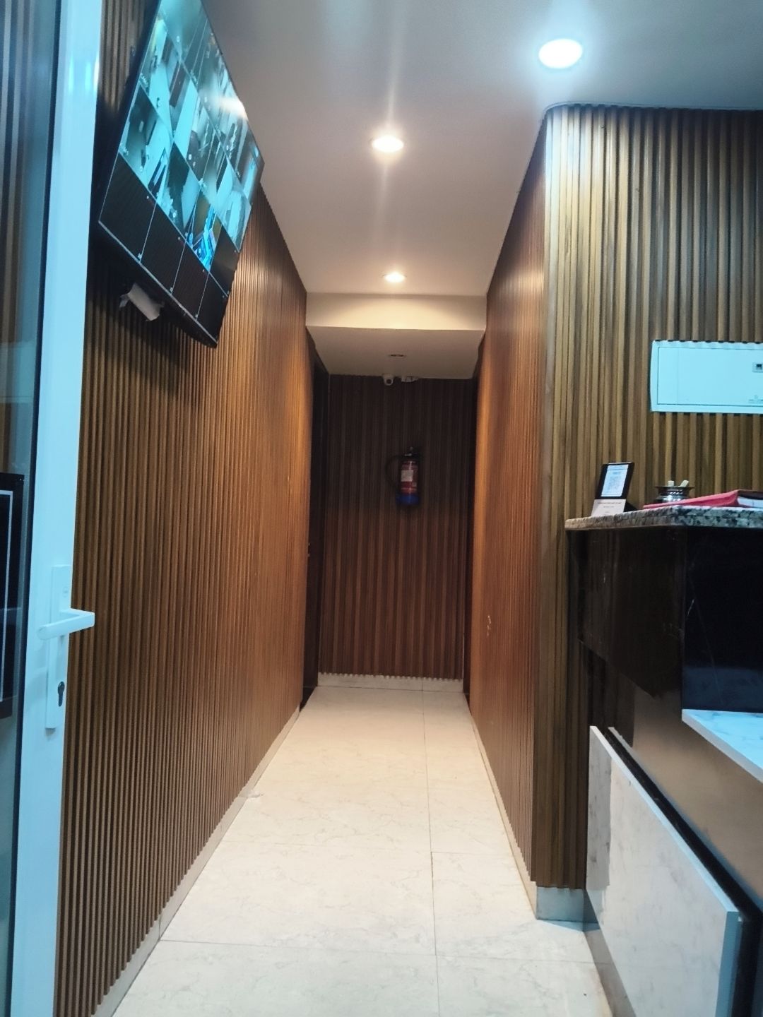 A hallway with wooden paneling, a fire extinguisher mounted on the wall, and a television mounted on the left wall.
