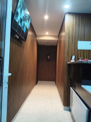 A hallway with wooden paneling, a fire extinguisher mounted on the wall, and a television mounted on the left wall. - Hotel Black Rose Near Rajiv Gandhi Cancer Hospital (New Delhi)