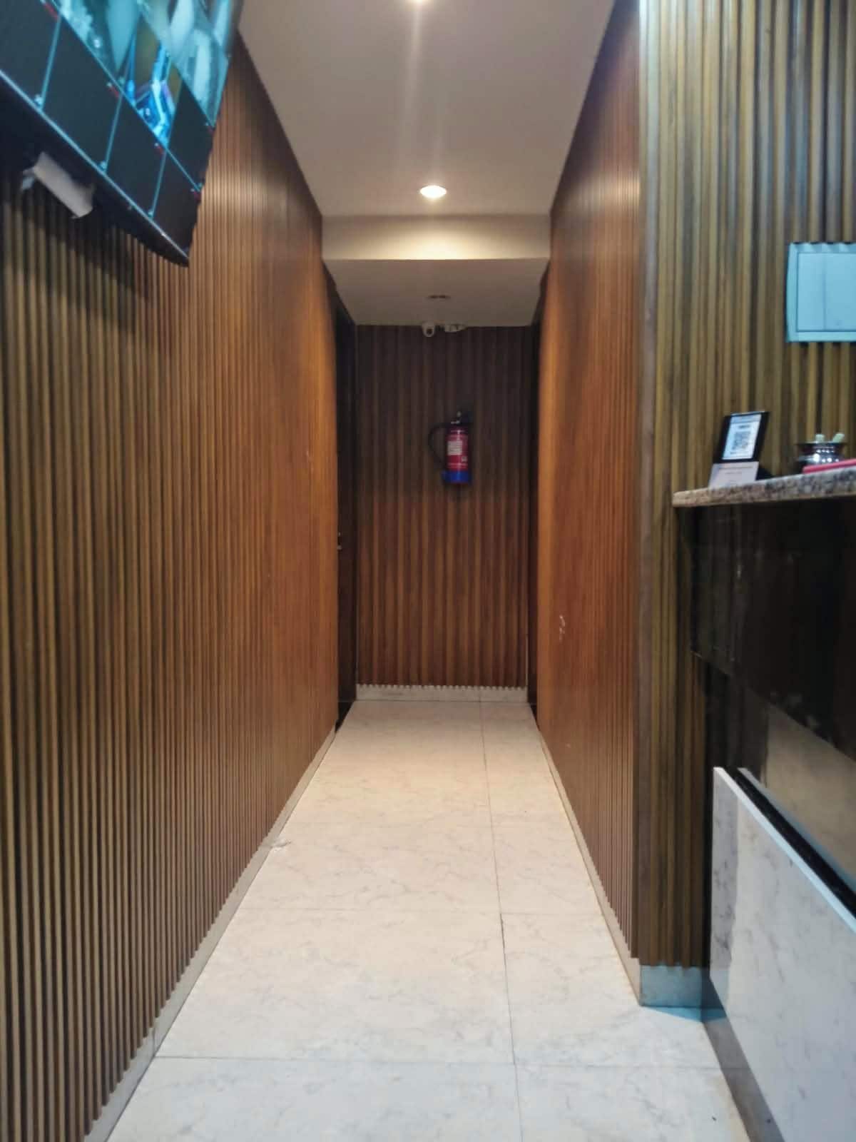 A corridor with wooden paneling on the walls, a tiled floor, a ceiling light, and a fire extinguisher mounted on the wall.