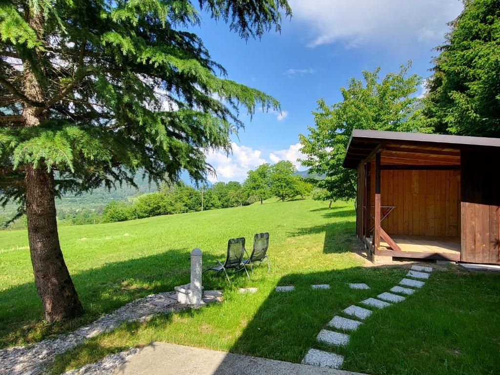 Une cabane en bois avec un sentier de pierres menant à deux chaises, le tout entouré d’une végétation luxuriante et sous un ciel dégagé.