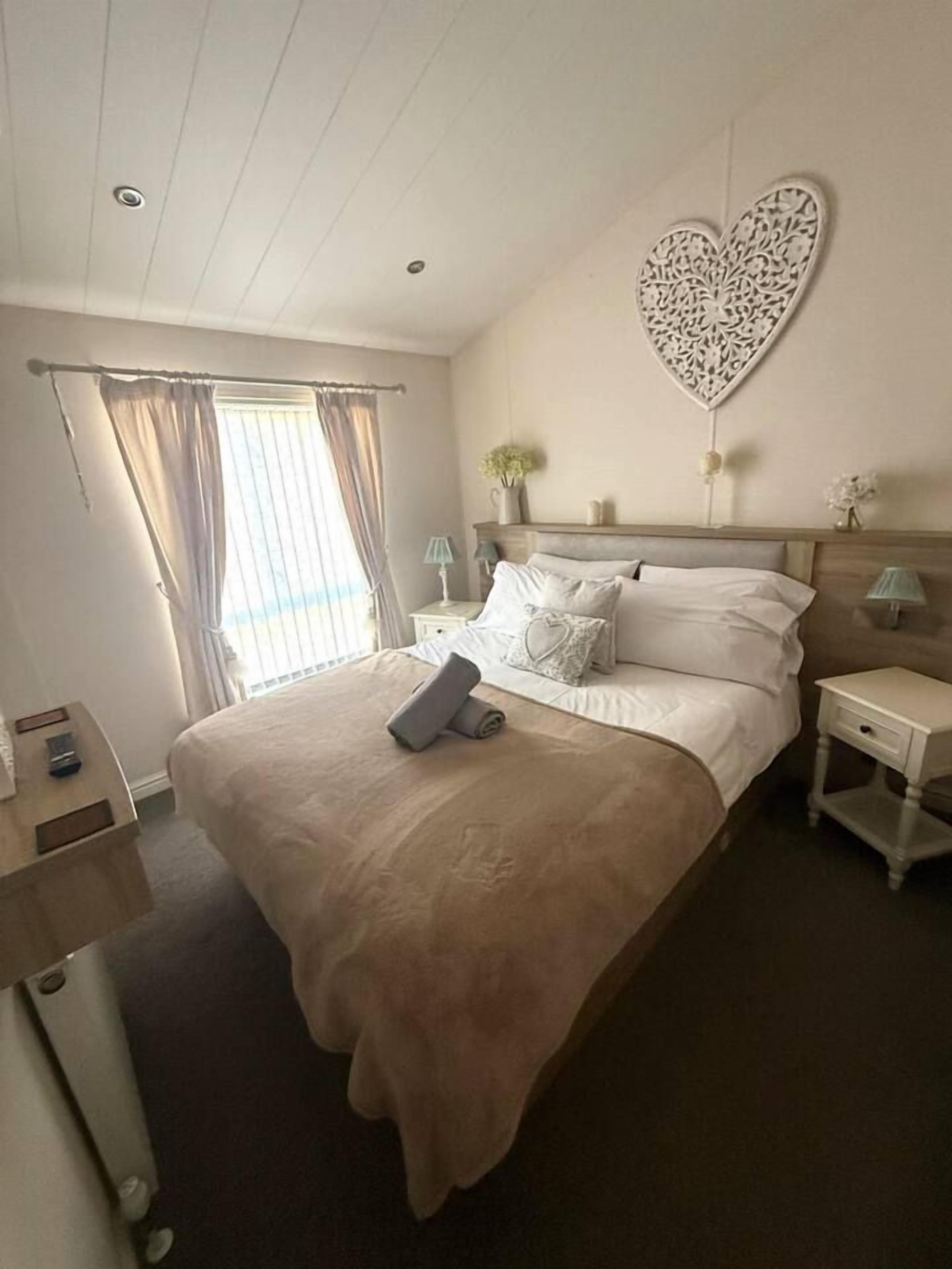 Ein Hotelzimmer mit einem großen Bett, einem Nachttisch, einer Lampe und einem dekorativen Wandelement in Herzform.