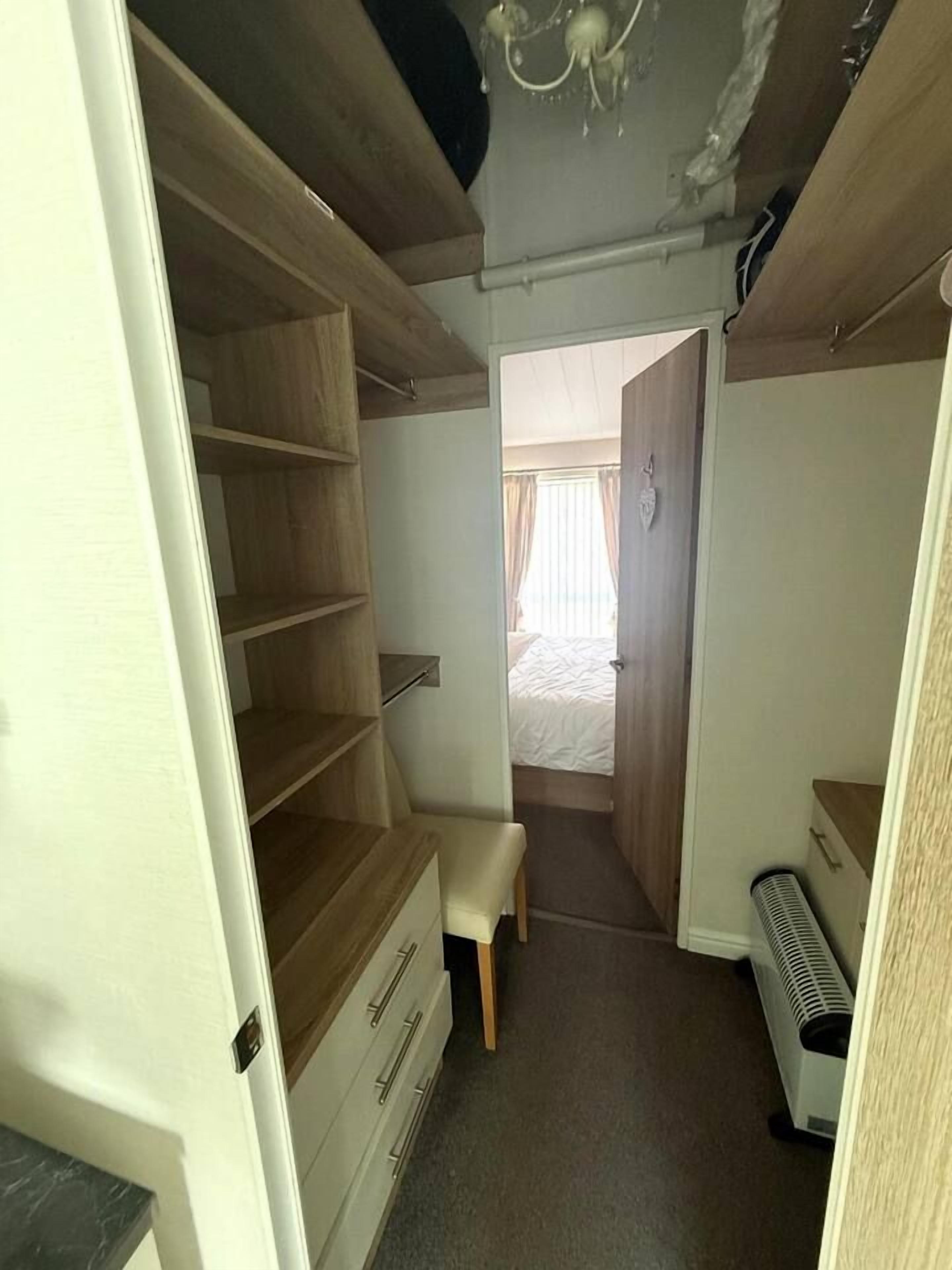 Un pasillo estrecho con un banco de madera, un radiador y una cama visible a través de una puerta abierta.