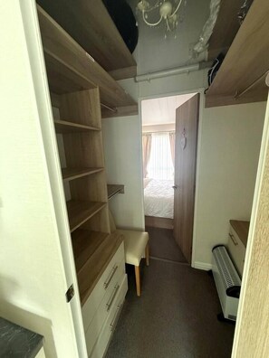Un passadís estret amb una banca de fusta, un radiador i un llit visible a través d'una porta oberta.
