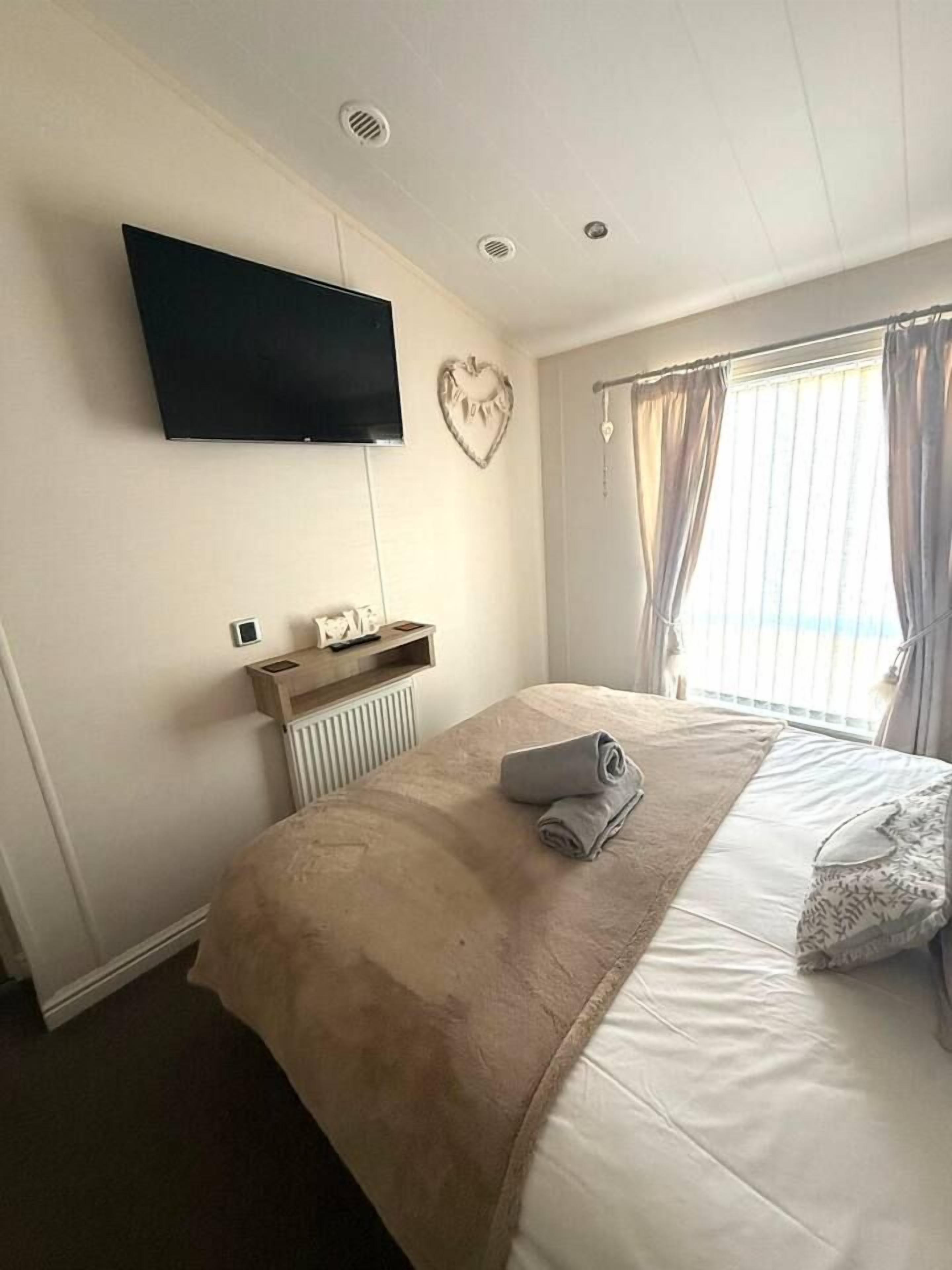 A hotel room with a bed, a flat-screen TV mounted on the wall, a radiator, and a window with curtains.