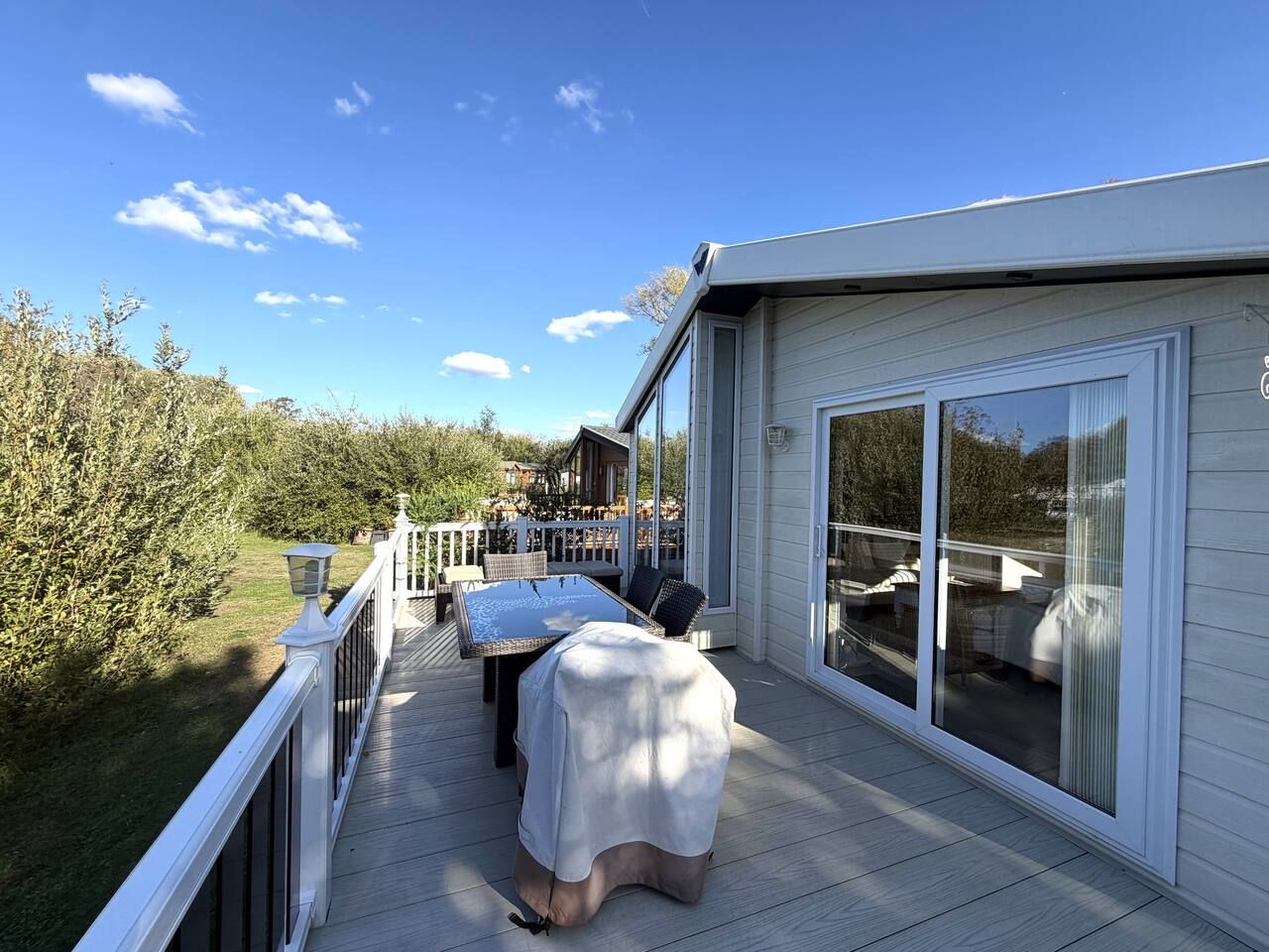 A covered outdoor deck with a table and chairs, a sliding glass door, and a view of the surrounding landscape.