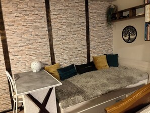 A modern living room with a stone wall, a white sofa with patterned cushions, a small table, and a decorative tree wall art piece.