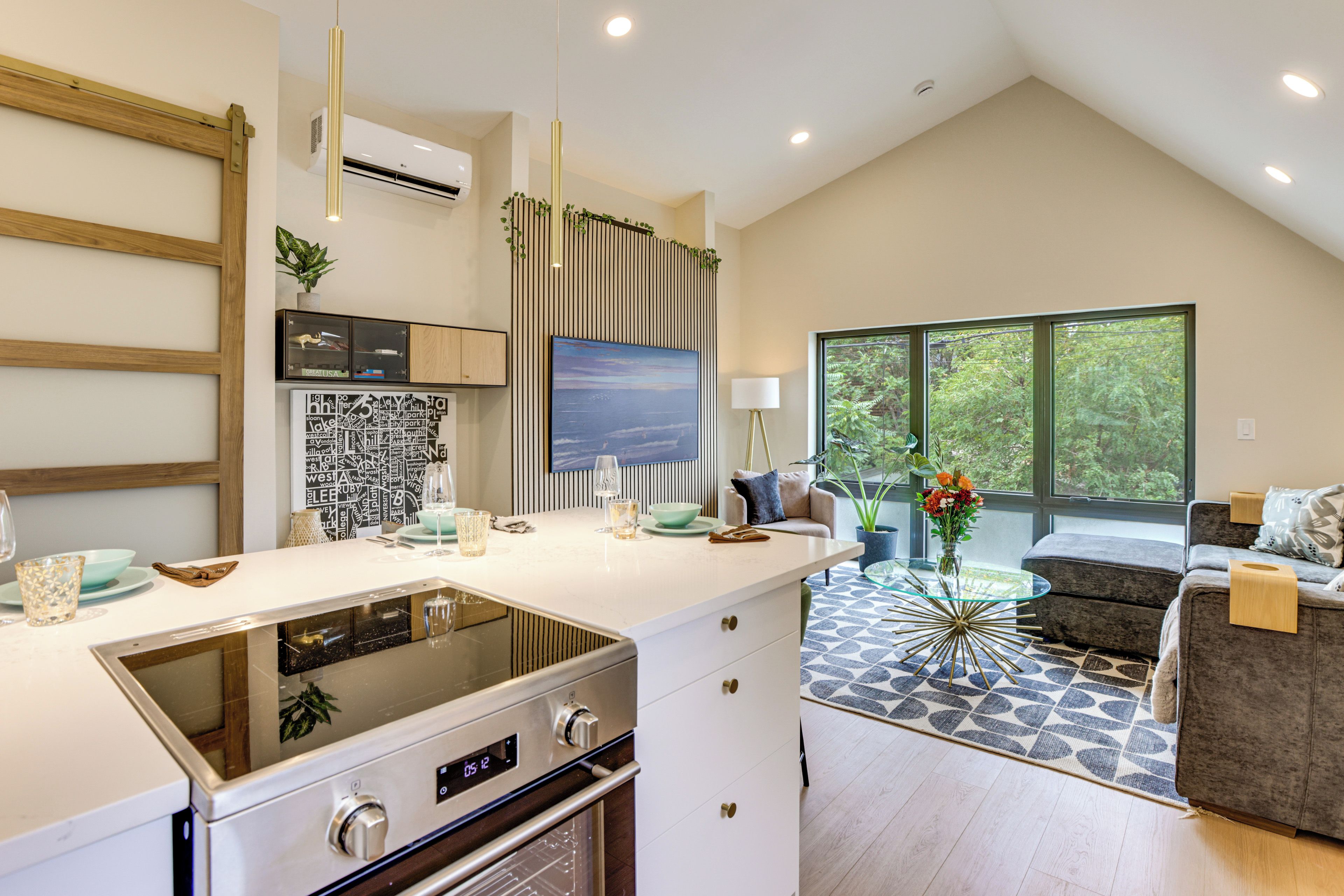 A modern kitchen with a built-in oven, a dining area with a glass table, and a view of the outdoors through large windows.