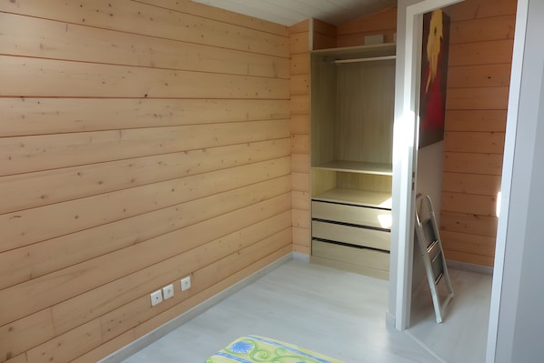 Een kamer met houten wanden en een witte vloer, met een inloopkast met schuifdeuren en een metalen ladder.
