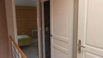 Un couloir au plancher de bois mène à une pièce où se trouvent un lit et une fenêtre.