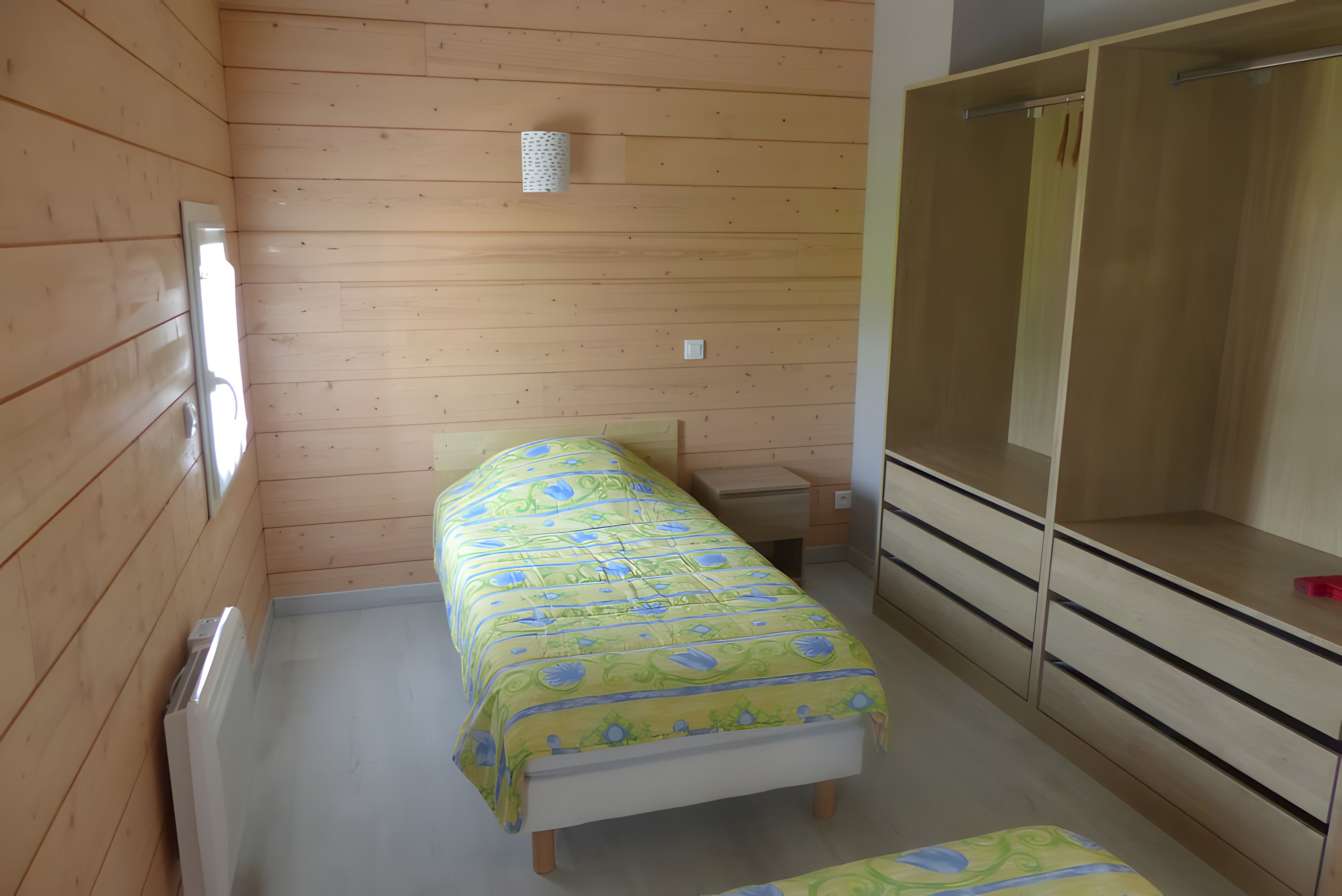 A small, single-bed room with wooden walls and a simple bed.