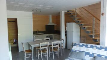 A modern kitchen with a central island, a dining area with wooden chairs, and a staircase leading to an upper level.