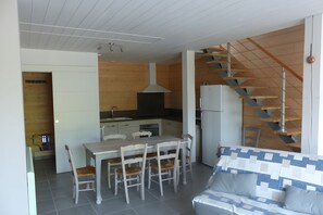 Een moderne keuken met een centraal eiland, een eetgedeelte met houten stoelen, en een trap naar een hoger niveau.