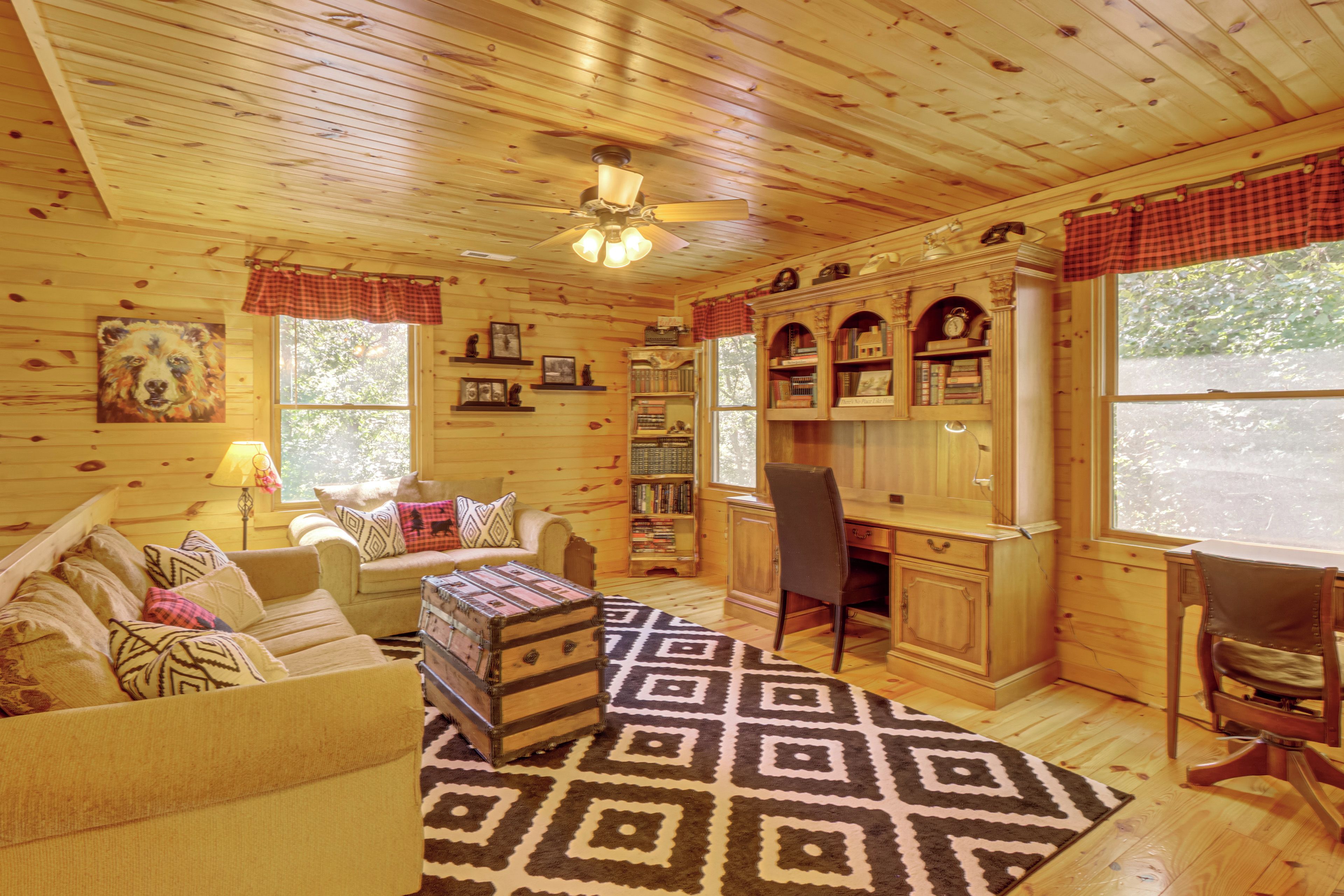 A cozy cabin interior with a wooden ceiling, a sofa, a desk, and a bookshelf.