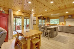 A wooden cabin interior with a dining area, kitchen, and large windows.