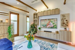 Een moderne woonkamer met een flatscreen televisie, houten balken, een groot raam en een kamerplant.