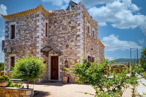 A stone building with a traditional design, featuring a central entrance with a small porch, and a clear sky in the background. - Liokrina Villa Elia - Livadakia Poolside Gem (Λιβαδάκια)