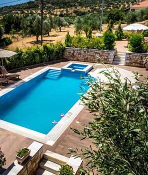Ein rechteckiger Pool mit Steinumrandung und Stufen, umgeben von viel Grün und Blick auf eine hügelige Landschaft.