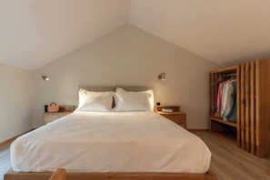 Ein Schlafzimmer mit einem großen Bett, einem Holzkopfende, Nachttischen, einem Schrank aus Holz und einer schrägen Decke.