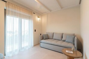 En moderne stue med en sofa, et glasbord og lette gardiner.