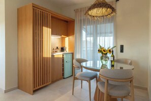 A compact kitchen with a built-in cabinet, a small refrigerator, and a dining area with a round table and two chairs. - Liokrina Suite 06 - Livadakia Poolside Getaway! (Livadakia)