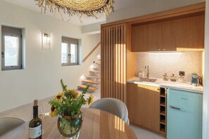 A modern kitchen with wooden cabinets, a built-in refrigerator, and a dining area with a table and chairs. - Liokrina Suite 06 - Livadakia Poolside Getaway! (Livadakia)