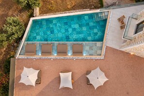 Eine Vogelperspektive auf einen Swimmingpool mit Sonnenterrasse, umgeben von einer Steinmauer und mit Sonnenschirmen ausgestattet.