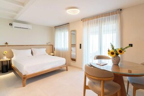 Een hotelkamer met een bed, nachtkastje, lamp, spiegel, en een zithoek met stoelen en een tafel.