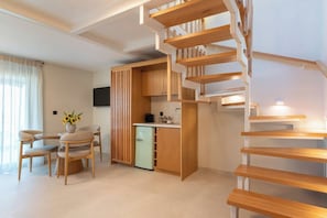 A modern interior with a central dining area, a kitchen with wooden cabinets, and a spiral staircase. - Liokrina Suite 05 - Livadakia Poolside Getaway! (Livadakia)