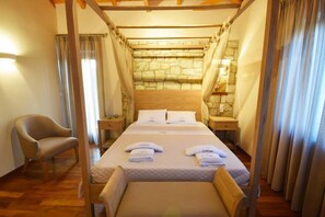 Un dormitorio con cama con dosel, cabecera de madera, mesita de noche con lámpara, una silla y pared de piedra.