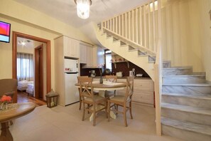 A dining area with a round table and chairs, a kitchen with white cabinets, and a marble staircase. - Liokrina Villa Hellios - Livadakia Poolside Gem (Λιβαδάκια)