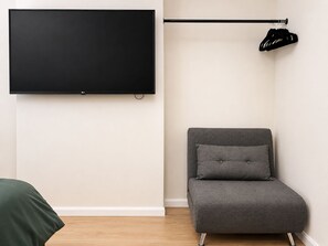 A room with a flat-screen TV mounted on the wall, a grey sofa with a pillow, and a black coat rack with a coat. - Access Great Venues, Airports, cLDN, Tottenham hale station apartment W/Parking! (London)