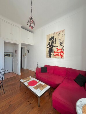Un soggiorno con un divano rosso, un tavolino e una locandina appesa al muro.