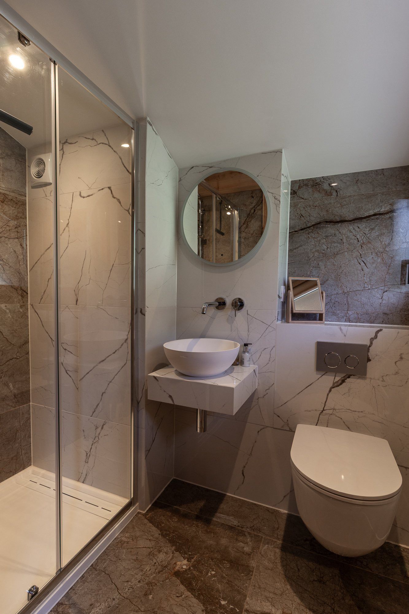 Une salle de bain dotée d’une douche à parois de verre, d’un lavabo avec un plan de travail en marbre, de toilettes et d’un miroir mural.
