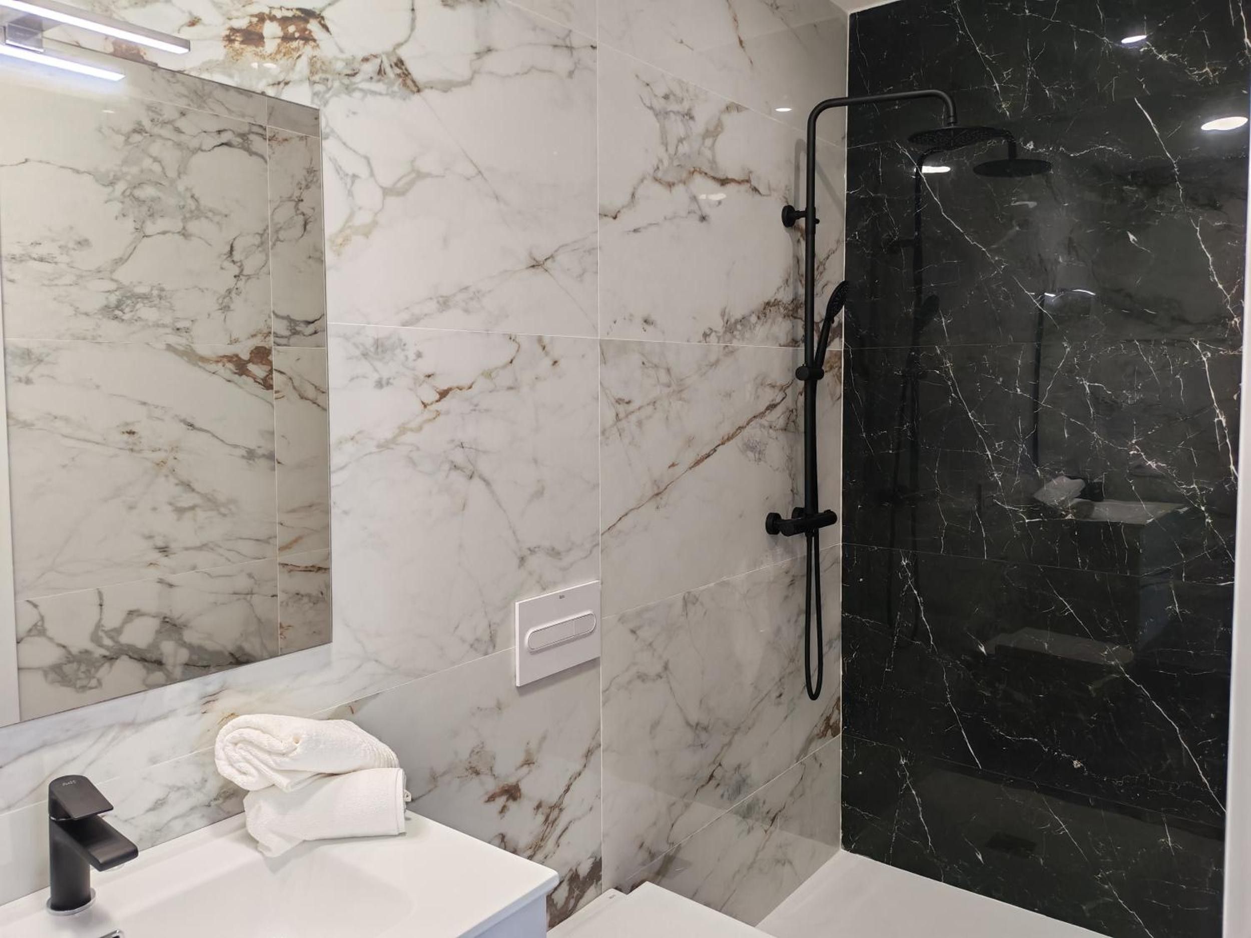 Un baño con pared de mármol, cabina de ducha de vidrio y lavabo blanco.