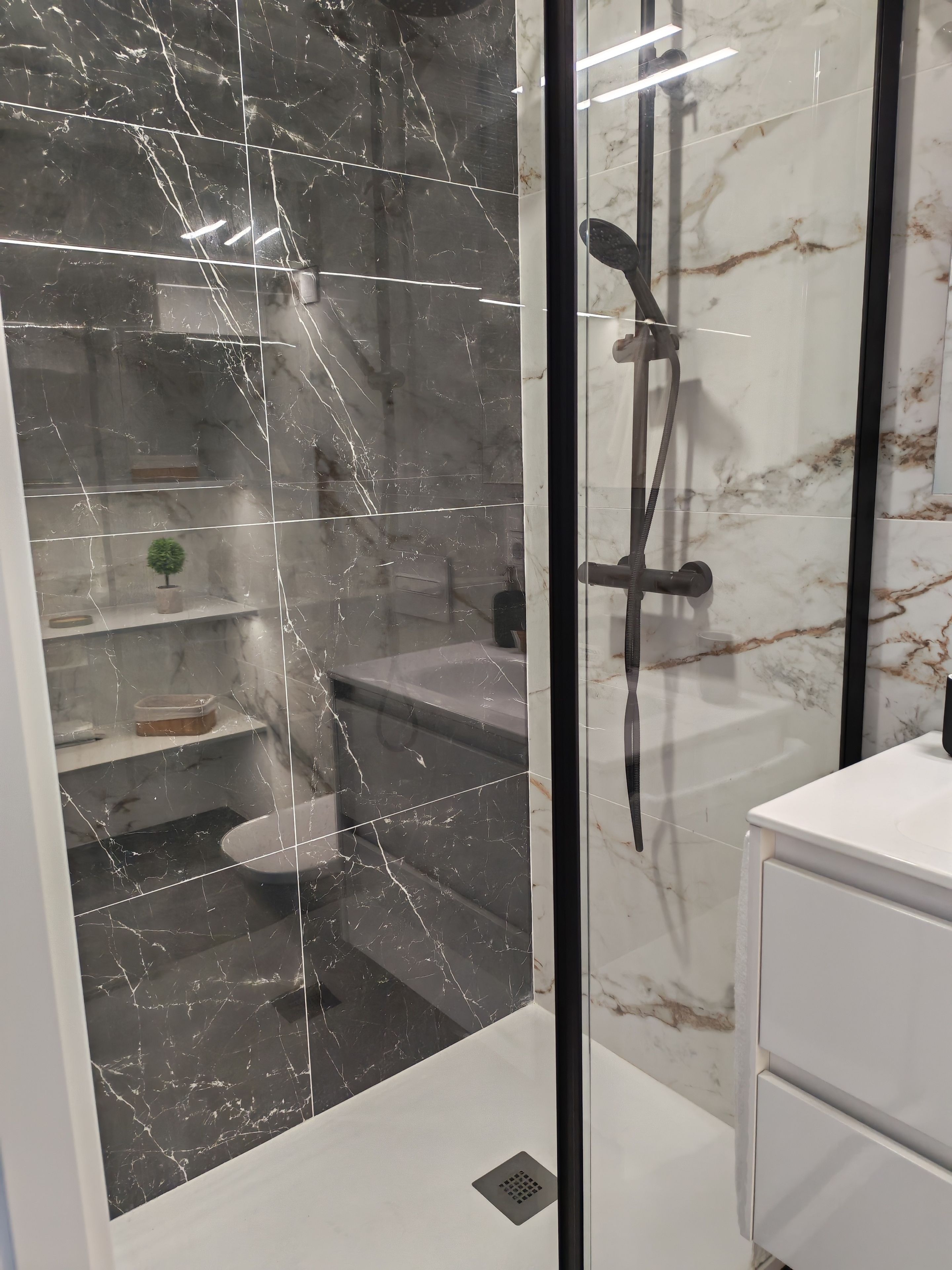 Un baño con ducha envuelta en vidrio, azulejos de mármol, un inodoro y un lavabo.