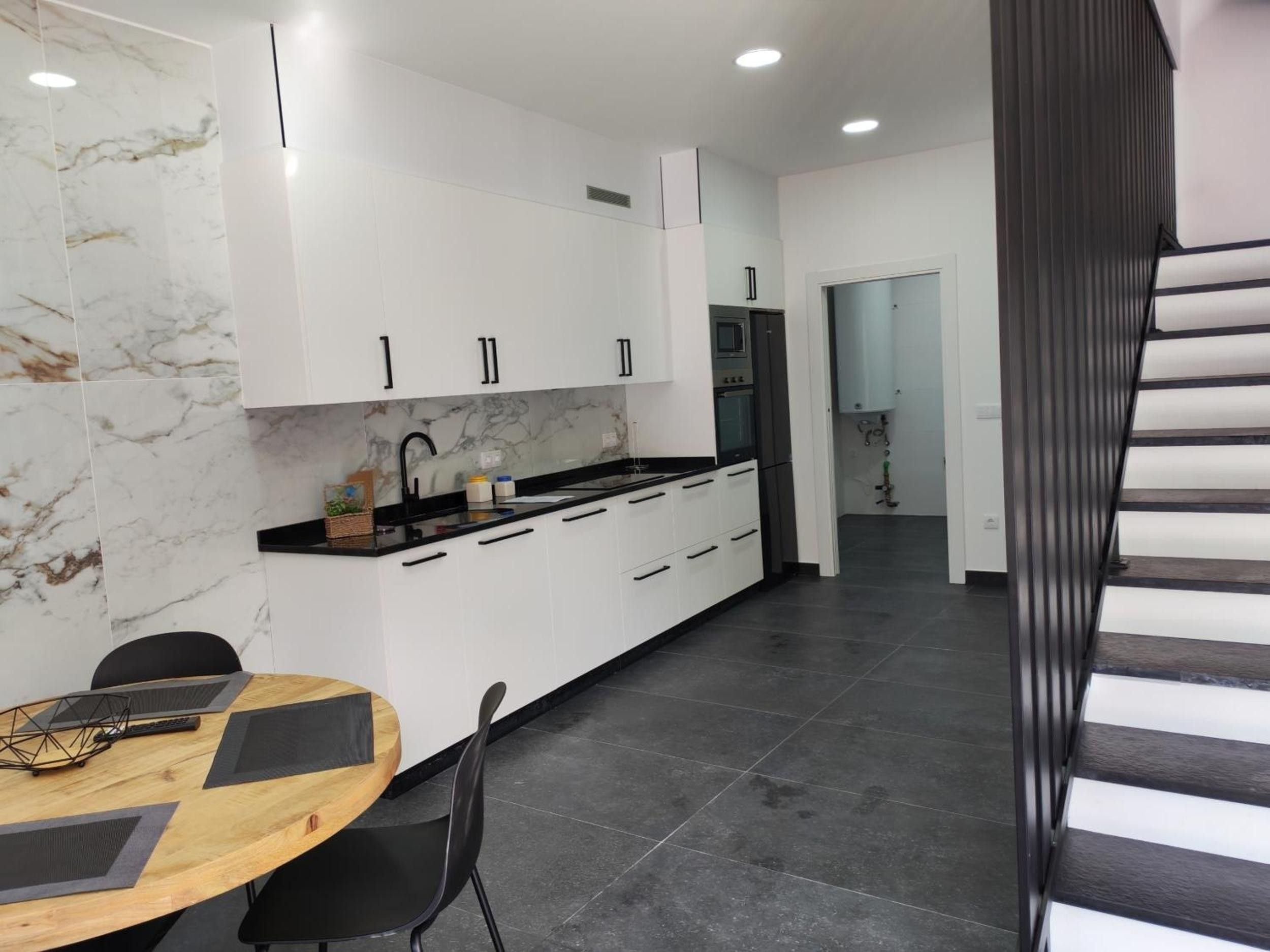 Una cocina moderna con armarios blancos, salpicadero de mármol y encimera negra.