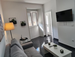 A modern living room with a grey sofa, a white coffee table, a flat-screen TV, and a lamp.