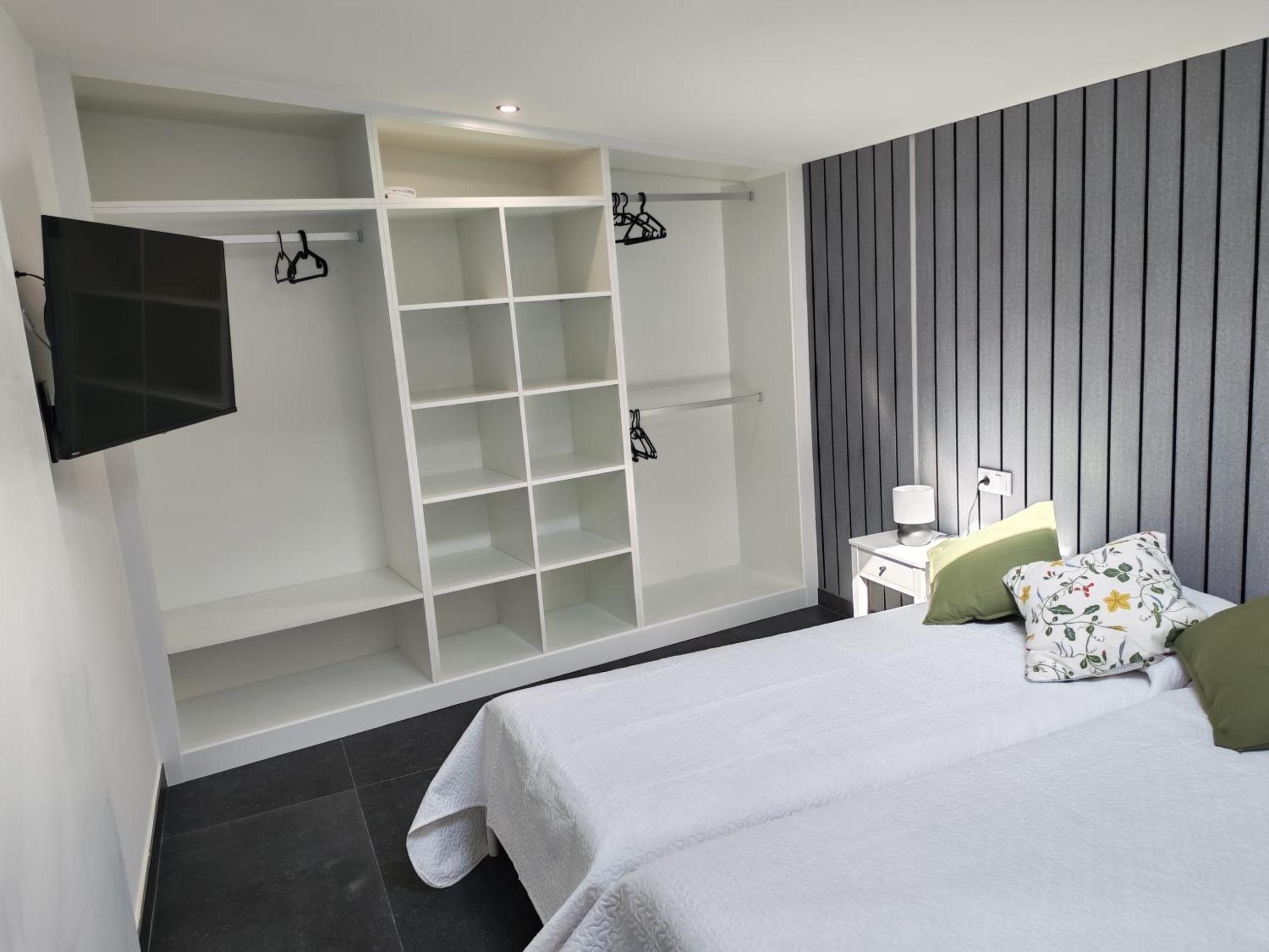Un dormitorio con cama, armario, mesita de noche y televisor.