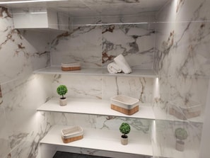 A bathroom with marble walls, multiple shelves, and a small potted plant.